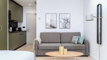 A modern living room with a grey sofa, two framed pictures on the wall, a round coffee table with two candles, and a minimalist lamp.