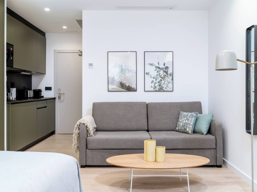 A modern living room with a grey sofa, two framed pictures on the wall, a round coffee table with two candles, and a minimalist lamp.