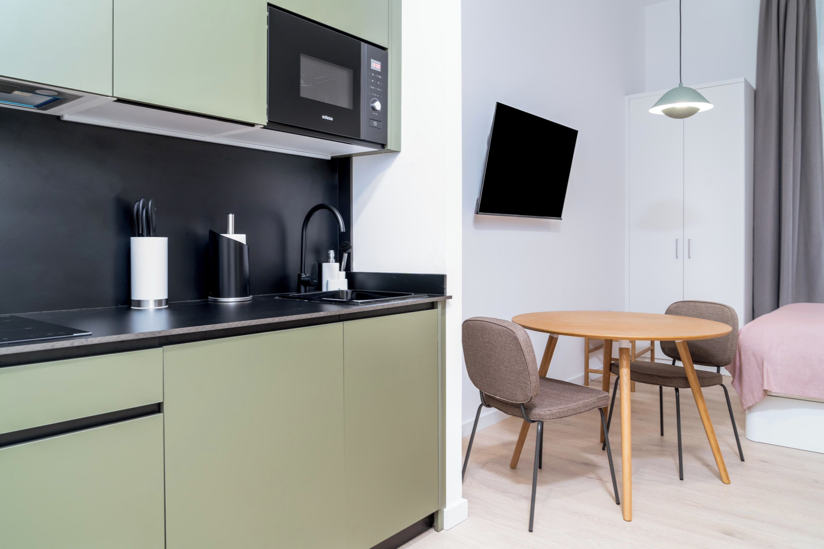 A modern kitchen with a microwave, coffee maker, and utensils on the counter. There is a dining area with a table and chairs.