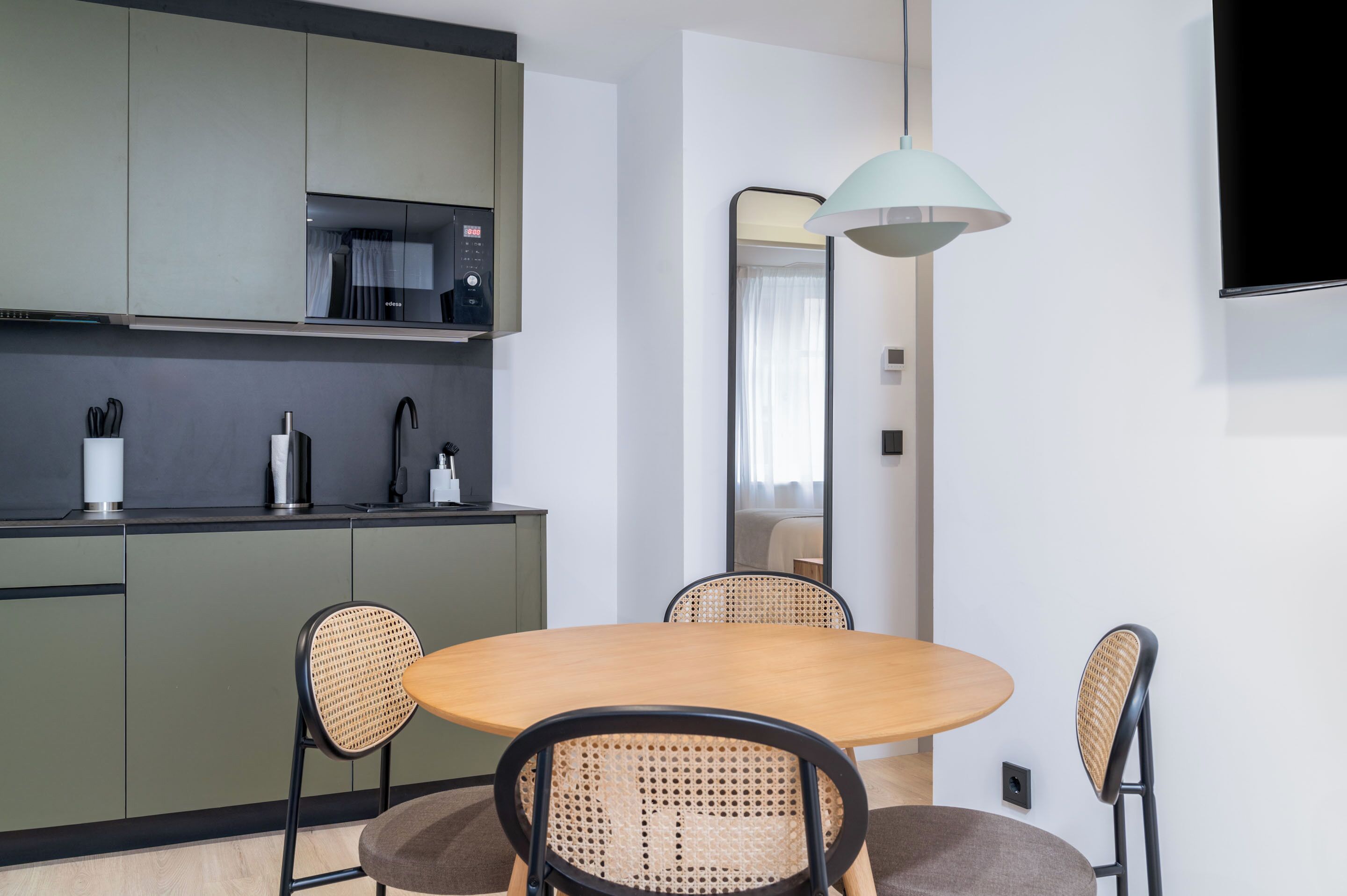 Una cocina moderna con armarios verdes, un grifo negro y una mesa de comedor de madera con cuatro sillas de mimbre.