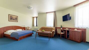 Quarto de hotel com cama, sofá, escrivaninha e televisão.