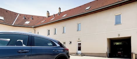 A modern building with a red-tiled roof, a car parked in front, and a gated entrance.