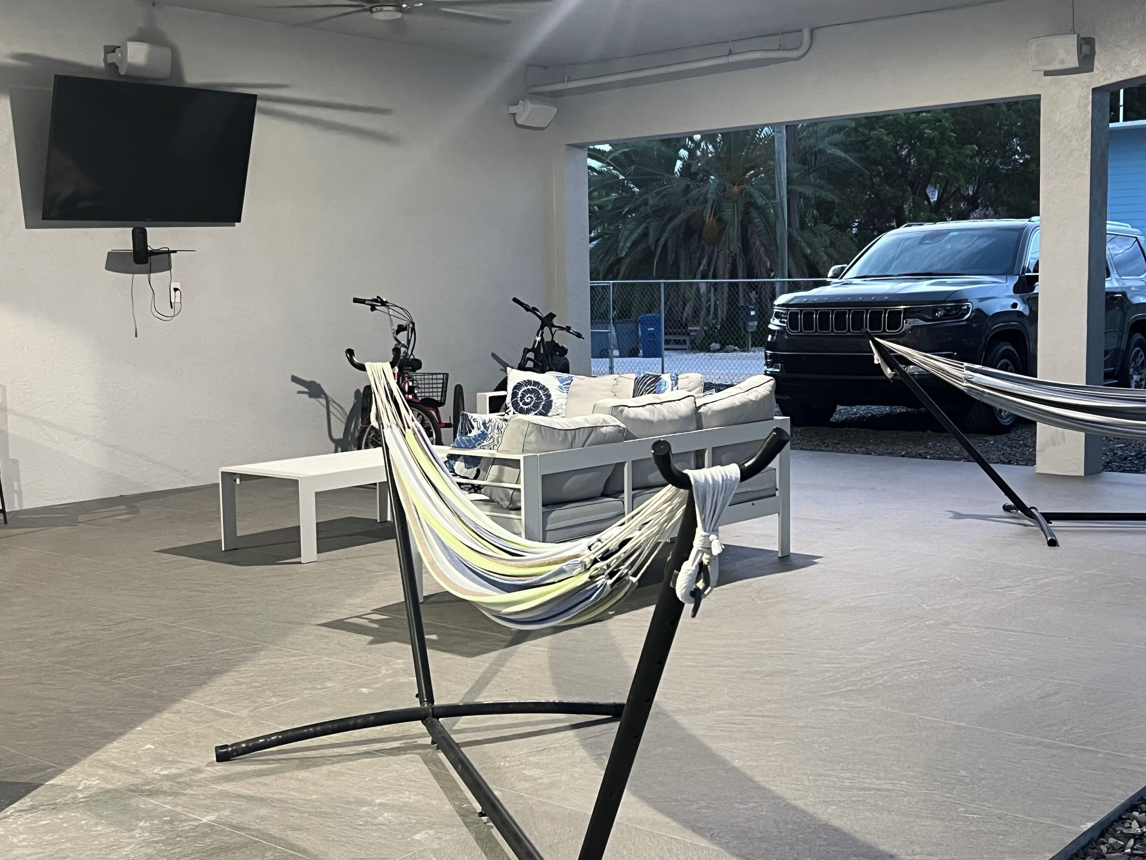 A modern interior with a large window, a white sofa, a hammock, and a car parked outside.