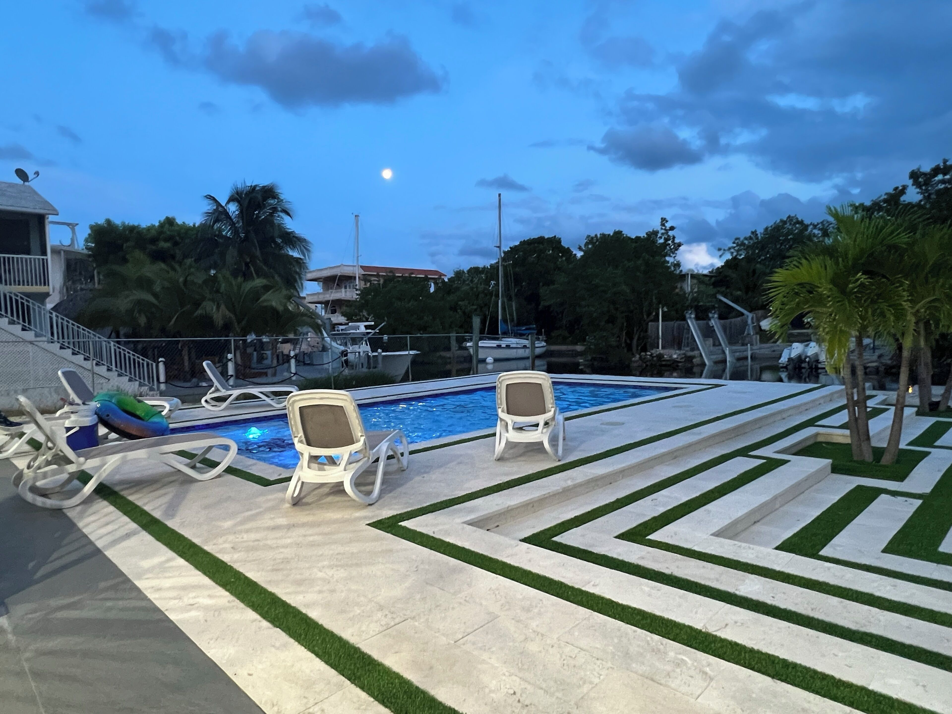 A pool area with two lounge chairs, a small boat, and a staircase leading to a building.