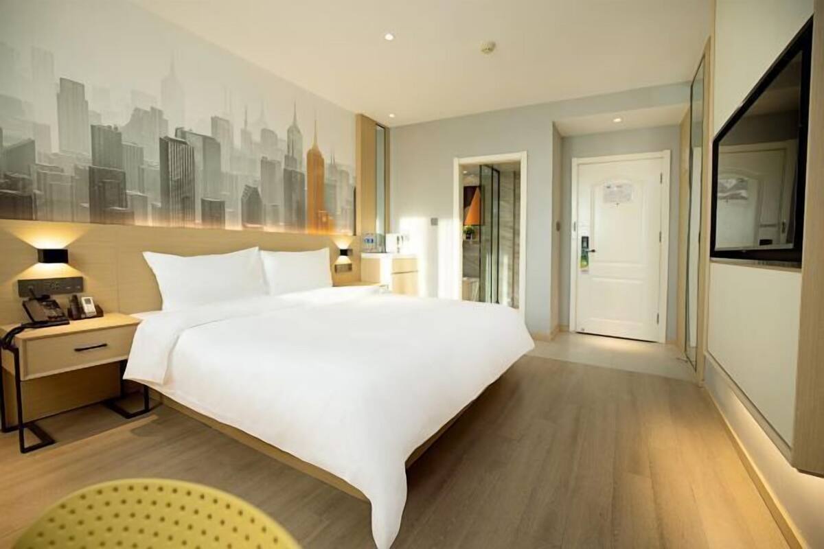 Habitación de hotel con una cama grande, mesitas de noche, un mural con un paisaje urbano, una puerta y un espejo.