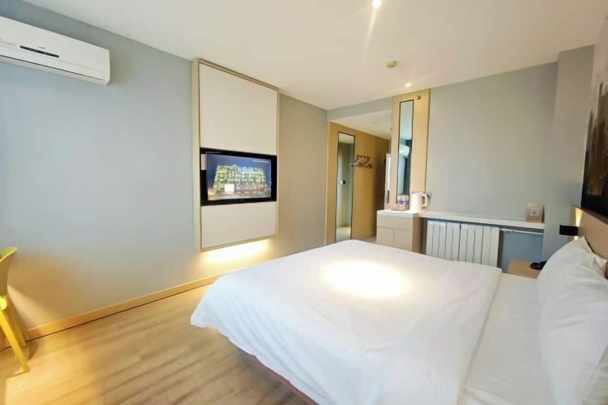 Una habitación de hotel con cama, televisión montada en la pared, mesita de noche y aire acondicionado.