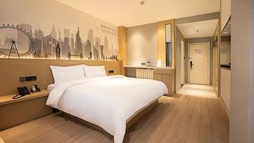 A hotel room with a bed, a nightstand, a mirror, a wall with a cityscape mural, and a hallway leading to a bathroom.