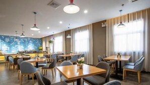 A modern dining area with multiple tables and chairs, a kitchen in the background, and large windows with curtains. - Songguo Hotel (Wenhua Road) (Zhengzhou)