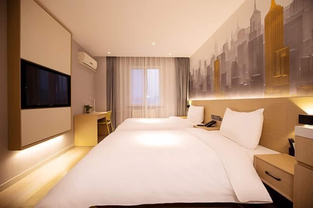 Una habitación de hotel moderna con una cama grande, mesitas de noche, un escritorio y un televisor montado en la pared.