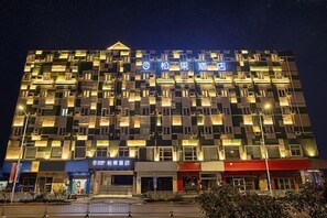 A multi-story hotel with a distinctive facade featuring numerous illuminated windows and balconies. - Songguo Hotel (Wenhua Road) (Zhengzhou)