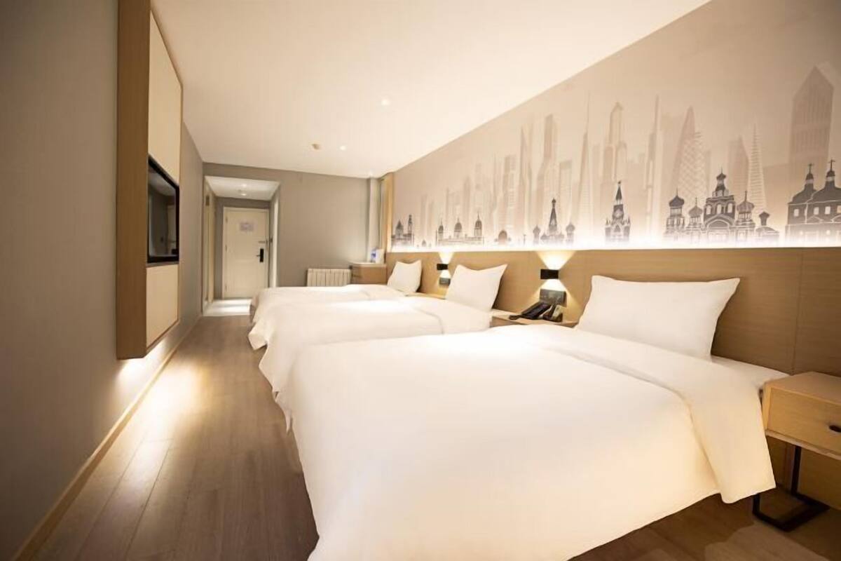 Habitación de hotel con dos camas, un mural con vista a la ciudad en la pared y piso de madera.