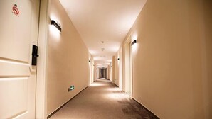 A long, narrow hotel corridor with beige walls and carpeted floors, featuring doors on both sides and a no-smoking sign on the left wall. - Songguo Hotel (Wenhua Road) (Zhengzhou)