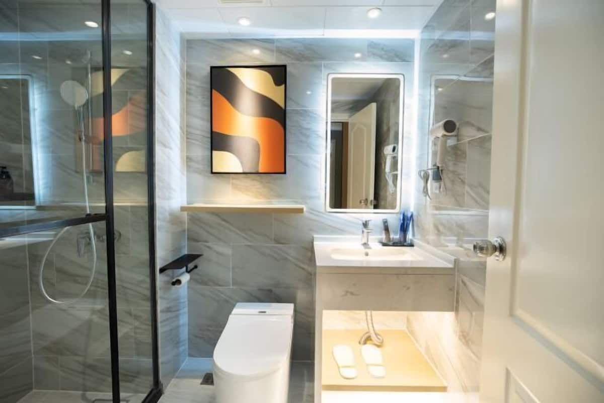 Un baño moderno con cabina de ducha de vidrio, inodoro, lavamanos con espejo y toallero.