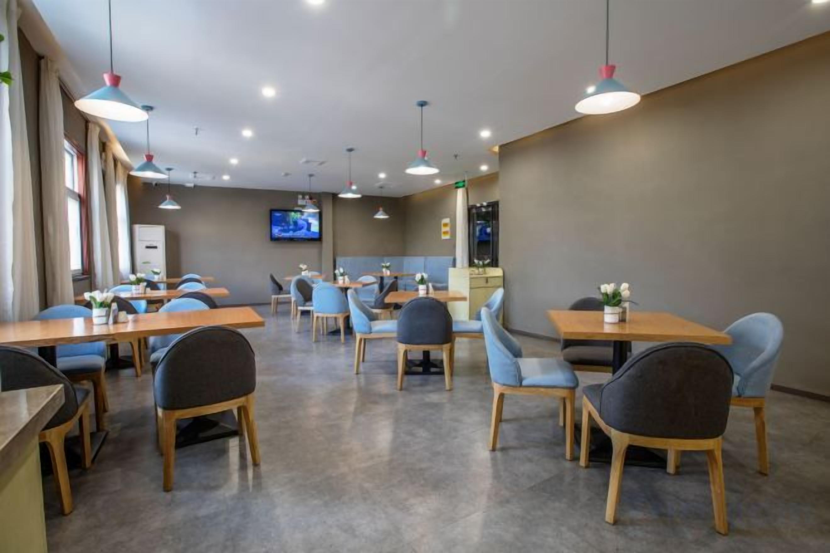 A restaurant with multiple tables and chairs, a television screen, and pendant lighting.