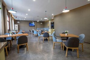 Un restaurante con varias mesas y sillas, una pantalla de televisión e iluminación colgante.
