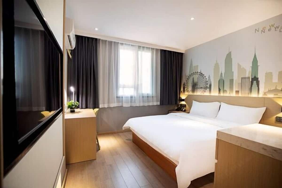 Una habitación de hotel con una cama, mesitas de noche, una ventana con cortinas, un mural con un paisaje urbano y vistas del horizonte de la ciudad.