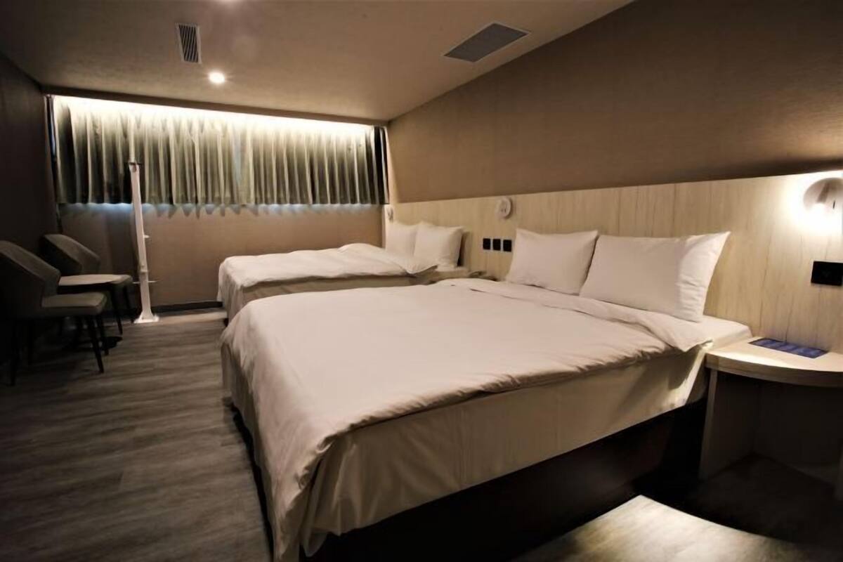 A hotel room with two beds, a desk, and a chair.