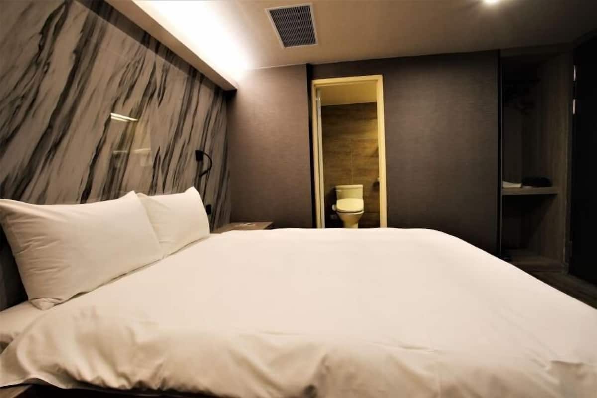 A modern hotel room with a large bed, a marble accent wall, and a walk-in closet.