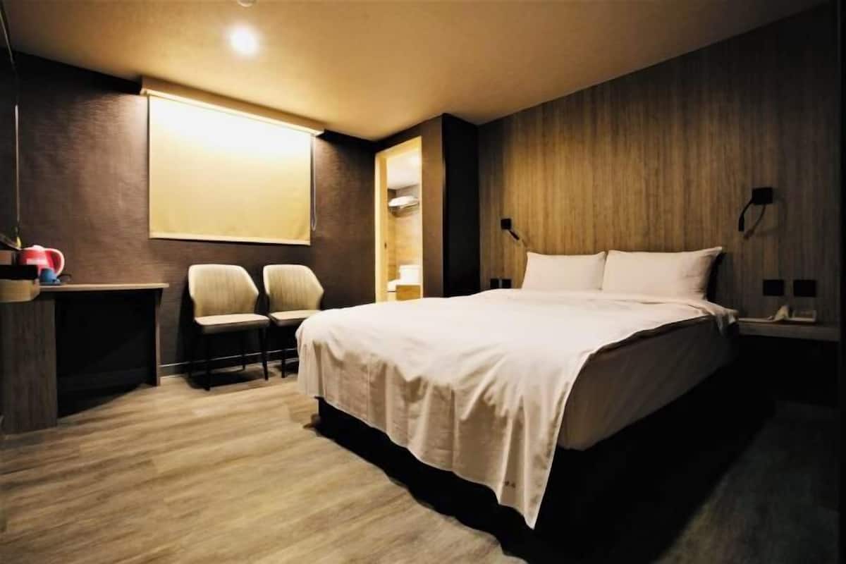 A modern hotel room with a large bed, two chairs, a desk, and a wooden accent wall.