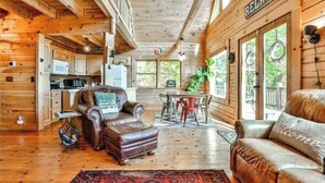 Interior acolhedor de uma cabana, com decoração em madeira, área de jantar e sala de estar com mobiliário de couro.