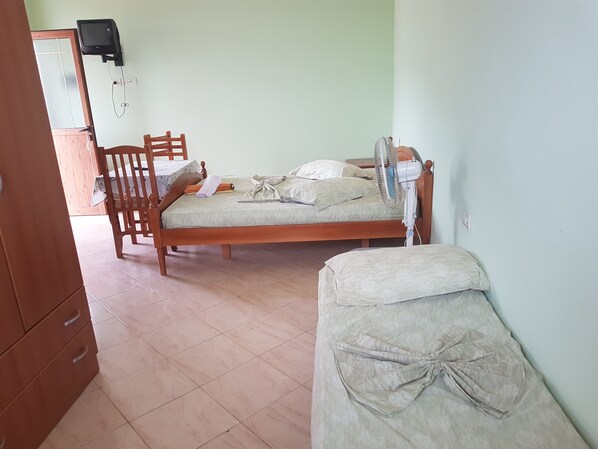 A bedroom with a wooden bed, a chair, a bedside table, and a small bedside fan.