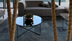 A modern living room with a sofa, a coffee table, and a view of the cityscape through large windows. - Studio na avenida 9 de julho (São Paulo)
