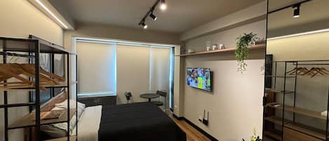 A modern hotel room with a bed, a TV, a desk, and a wardrobe.