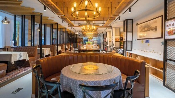 Ein Restaurant mit einem runden Tisch in der Mitte, Sitzecken und einer Holzbalkendecke.