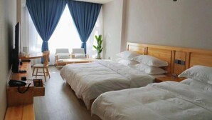 Ein Hotelzimmer mit zwei Betten, einem Schreibtisch, einem Sessel, einem Fernseher und einer Pflanze.