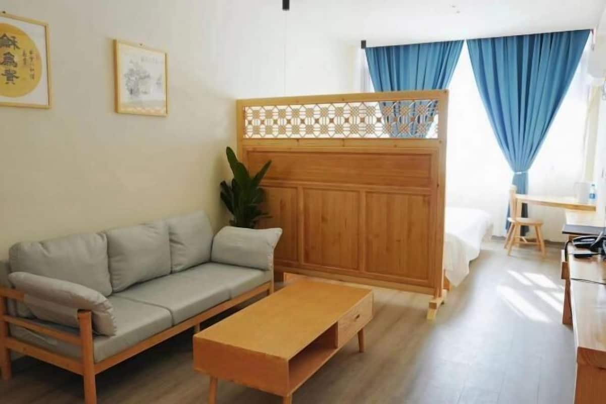 Ein Zimmer mit einem hölzernen Bett, einem Schlafsofa, einem kleinen Tisch und einem dekorativen Raumteiler.