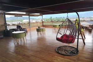 Un balcón amplio con una silla colgante, mesas redondas y vistas al paisaje.