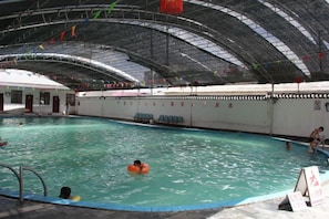 An indoor swimming pool with a high arched ceiling, clear water, and a few people swimming.