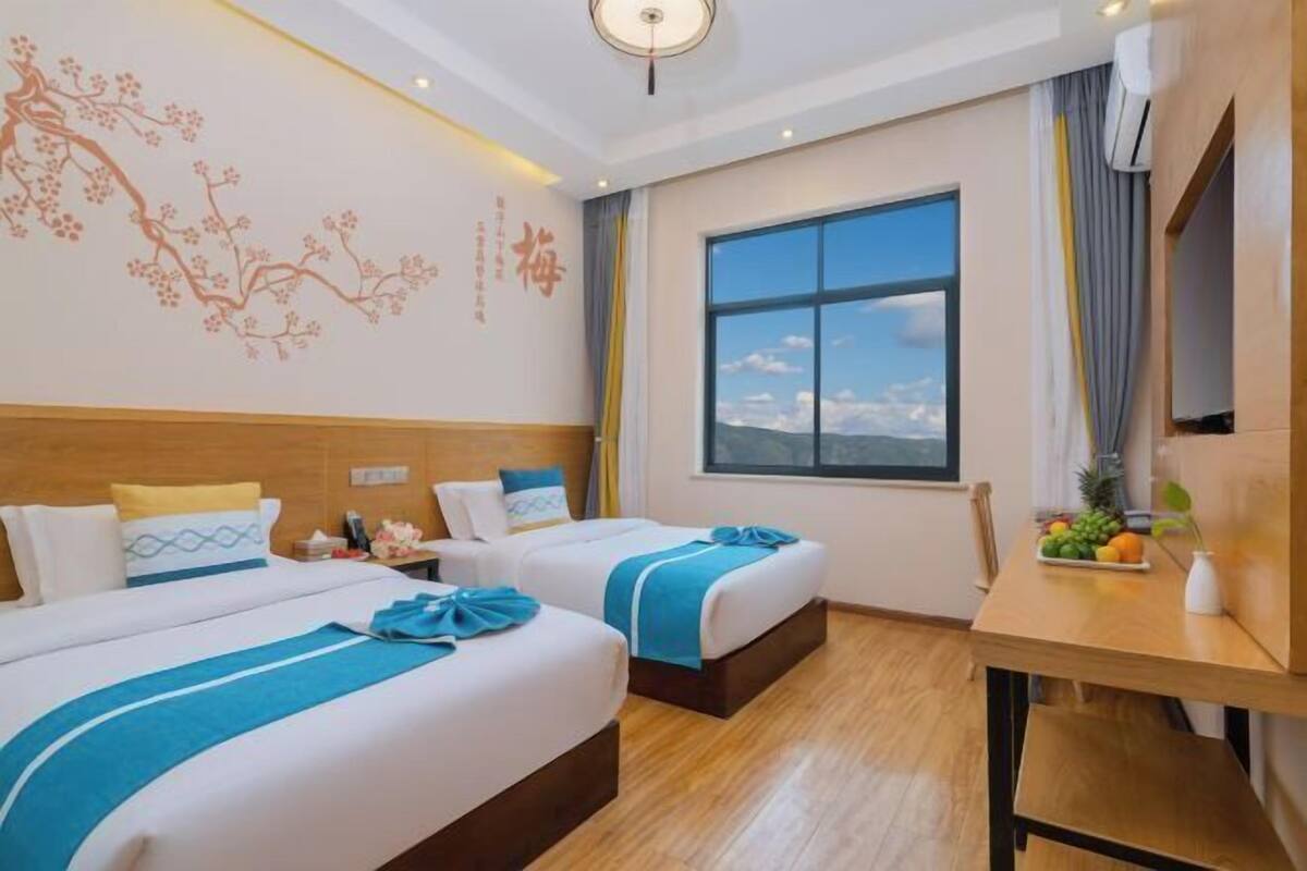 Ein Hotelzimmer mit zwei Betten, einem großen Fenster, einem Holztisch und einem dekorativen Wandbild.