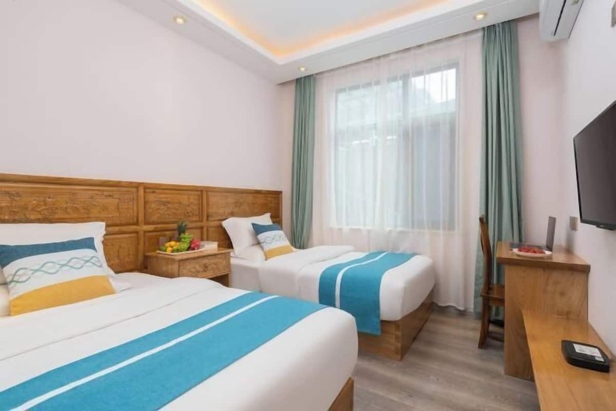 Ein Hotelzimmer mit zwei Betten, einem Holzkopfteil, einem Schreibtisch, einem Stuhl, einem Fernseher und einem Fenster mit Vorhängen.