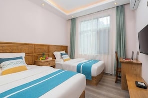 Habitación de hotel con dos camas, cabecera de madera, escritorio, silla, televisor y ventana con cortinas.