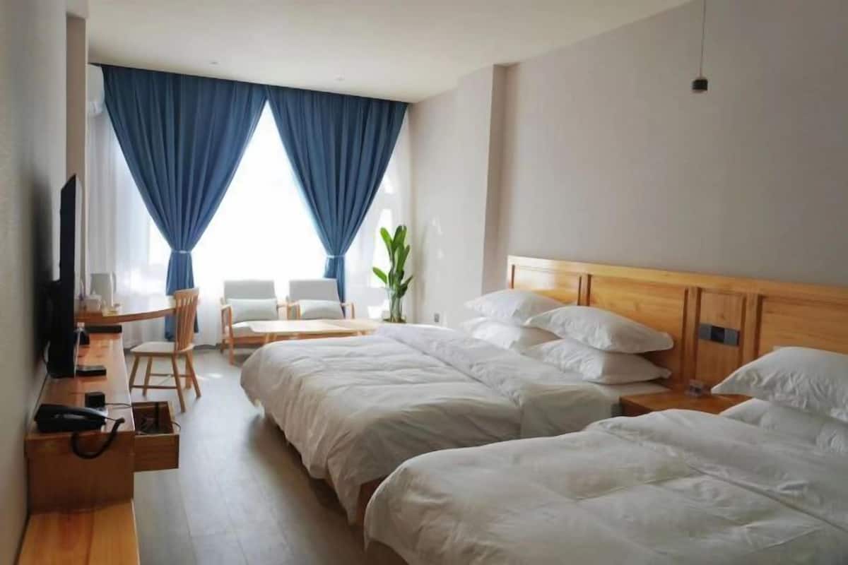 Ein Hotelzimmer mit zwei Betten, einem Schreibtisch, einem Sessel, einem Fernseher und einer Pflanze.