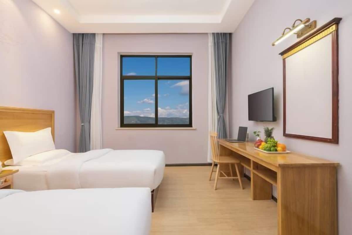 Ein Hotelzimmer mit zwei Betten, einem Schreibtisch mit Computer, einem Fernseher und einem großen Fenster mit Blick.
