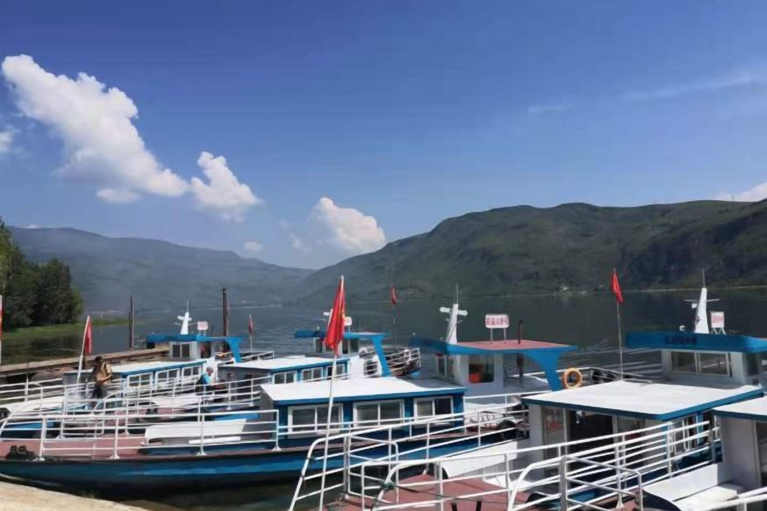 A marina with several boats docked, a clear sky, and mountains in the background.