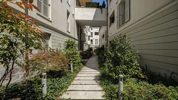 Un étroit passage bordé d’immeubles dotés de balcons, qui mène à un bâtiment central dont l’entrée est bien visible.