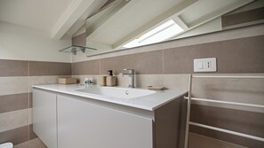 Une salle de bain moderne avec un lavabo blanc, des carreaux de couleur beige, une étagère en verre et un porte-serviettes.