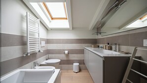 Une salle de bain moderne dotée d’une lucarne, d’une baignoire, de toilettes, d’un lavabo et d’un miroir.