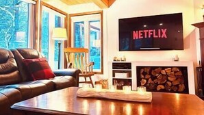 A cozy living room with a leather sofa, a coffee table, a fireplace, and a TV mounted on the wall displaying the Netflix logo. - Family chalet and SPA near Mont Orford (Orford)