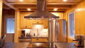 A modern kitchen with wooden cabinets, stainless steel appliances, and a central range hood. - Family chalet and SPA near Mont Orford (Orford)