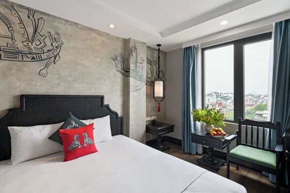 A hotel room with a large bed, a desk, a chair, a potted plant, and a view of the city through large windows. - 22land 52 Ngo Huyen Hotel & Spa (Hanoi)