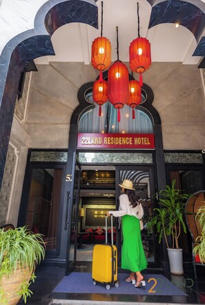 The entrance of 22Land Residence Hotel with a sign, a woman with a suitcase, and hanging lanterns. - 22land 52 Ngo Huyen Hotel & Spa (Hanoi)