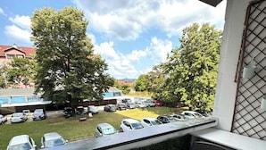 Un balcón con vista a coches estacionados y árboles, una silla y una mesa.