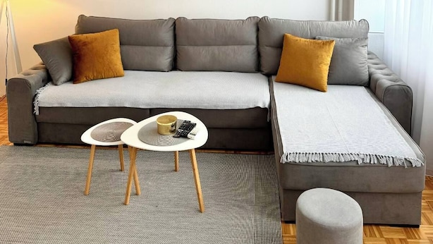 Una sala moderna con un sofá seccional gris, una mesita de centro redonda y un reposapiés gris.