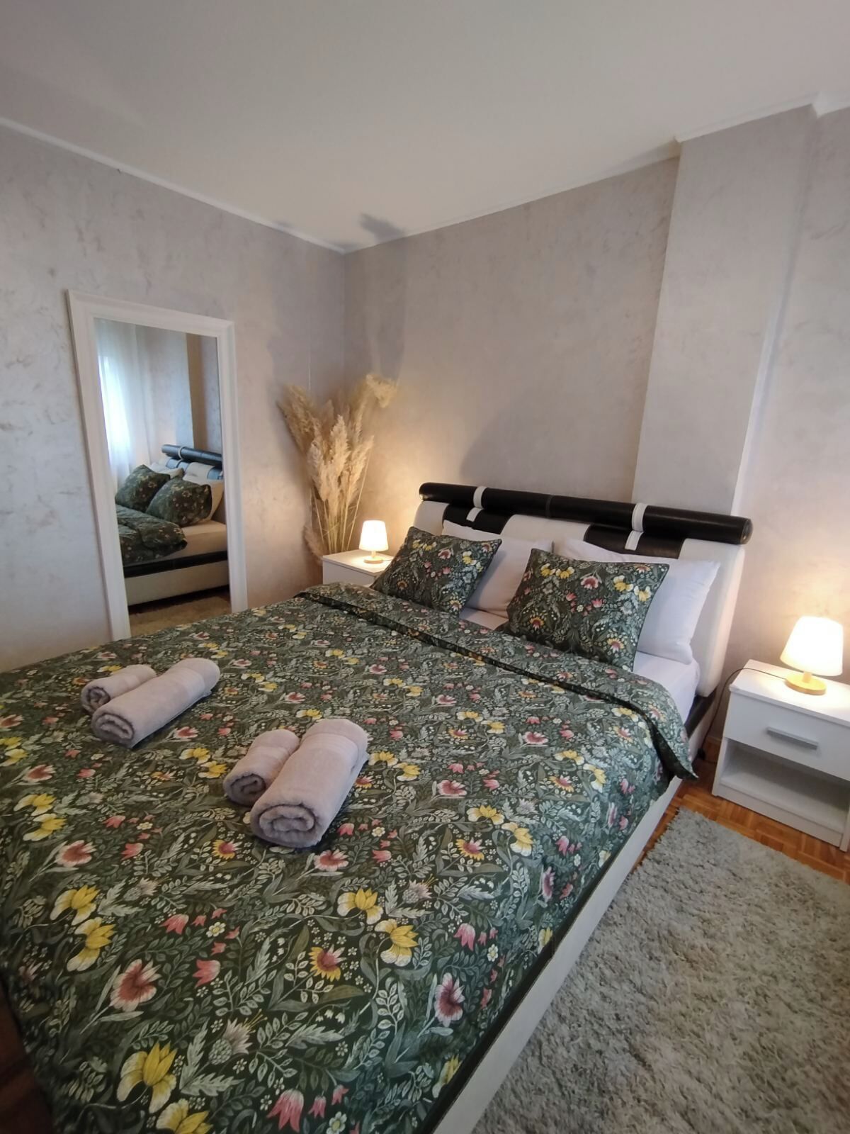 A bedroom with a large bed, two bedside tables, and a mirror.