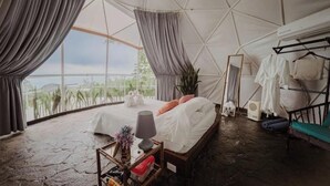 A tent-style room with a bed, a side table, a mirror, and a clothing rack. - AN AWESOME GLAMPING IN THE JUNGLE (Puntarenas Province)