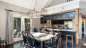 Une cuisine moderne avec des meubles de couleur sombre, un îlot central et un coin repas comprenant une grande table et des chaises.